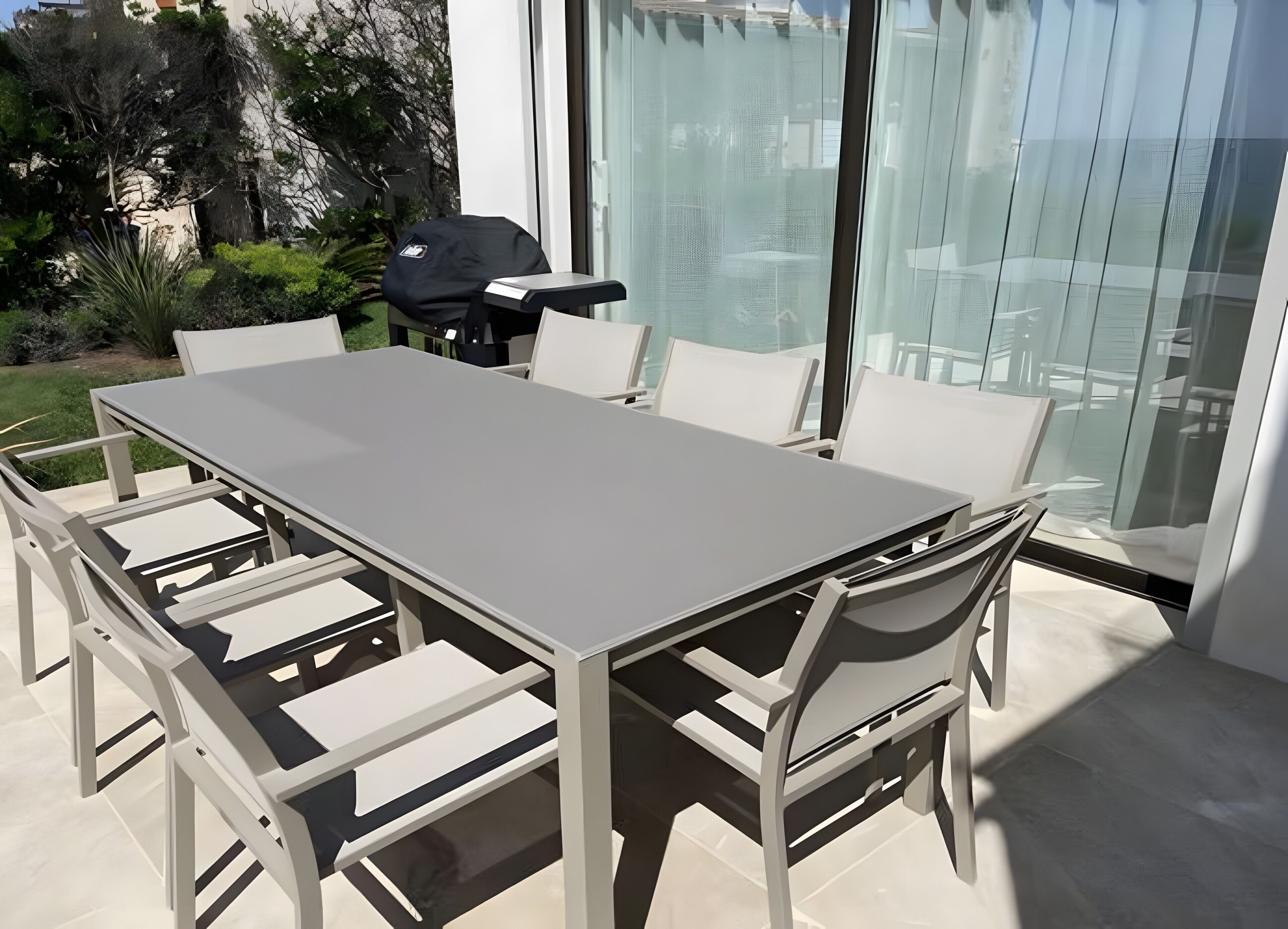 A modern outdoor dining area with a large table and chairs, a grill, and a view of the surrounding landscape.