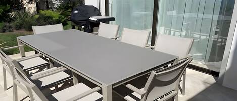 A modern outdoor dining area with a large table and chairs, a grill, and a view of the surrounding landscape.