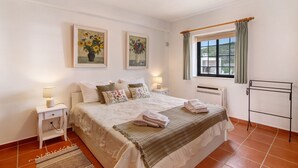 A bedroom with a bed, two bedside tables with lamps, a window with curtains, and two wall-mounted paintings. - Holiday Home 'Leo' with Sea View, Wi-Fi and Air Conditioning (Faro)