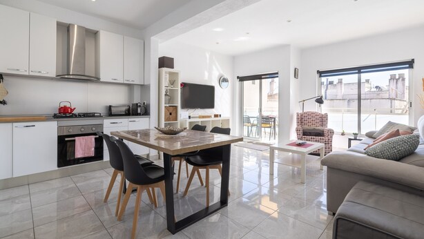 A modern kitchen with white cabinets, a stainless steel range hood, and a dining area with a wooden table and black chairs. - Apartment 'Mestral' with Balcony, Wi-Fi and Air Conditioning (Cambrils)