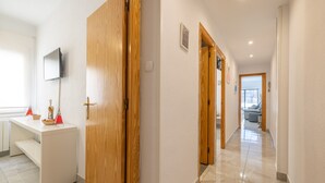 A hallway with wooden doors, a white desk with a television, and a glimpse of a living area in the distance. - Apartment 'Mestral' with Balcony, Wi-Fi and Air Conditioning (Cambrils)