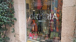 Un escaparate con un cartel que dice 'ORTIGIA SICILI' y una vitrina que exhibe varios artículos.