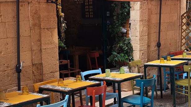 Un café al aire libre con paredes de piedra, mesas y sillas.