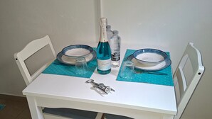 Et hvidt bord med to stole, en champagneflaske, to glas og to skåle på et flisebelagt gulv.