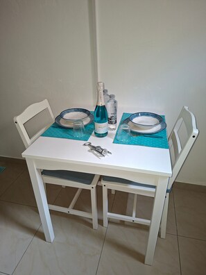 Une table blanche avec deux chaises, une bouteille de champagne, deux verres et deux bols posés sur un sol carrelé.