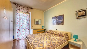 Ein Schlafzimmer mit Bett, Nachttisch, Kommode, einem Vorhang mit Meeresmotiv und einem Wandbild.