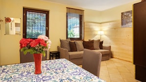 A living room with a sofa, a table with a patterned tablecloth, a vase with flowers, and a lamp. - Apartment 'Chateau Chatillon' with Mountain View, Private Terrace and Wi-Fi (Châtillon)