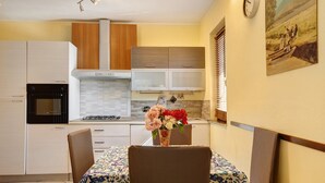 A compact kitchen with white cabinets, a stove, and a dining area with a table and chairs. - Apartment 'Chateau Chatillon' with Mountain View, Private Terrace and Wi-Fi (Châtillon)