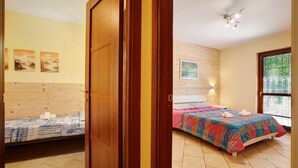 A bedroom with a wooden headboard, a bed with a colorful quilt, a window with blinds, and a painting on the wall. - Apartment 'Chateau Chatillon' with Mountain View, Private Terrace and Wi-Fi (Châtillon)