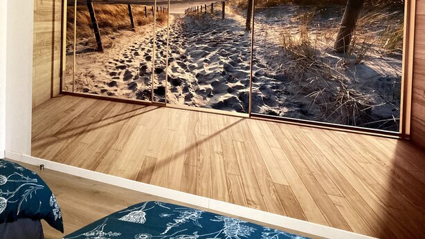 A room with a large panoramic window, wooden flooring, and a bed with a floral bedspread.