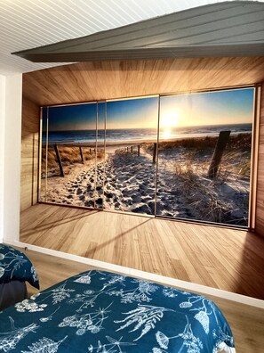 Ein Zimmer mit großem Panoramafenster, Holzboden und einem Bett mit floralem Überwurf.