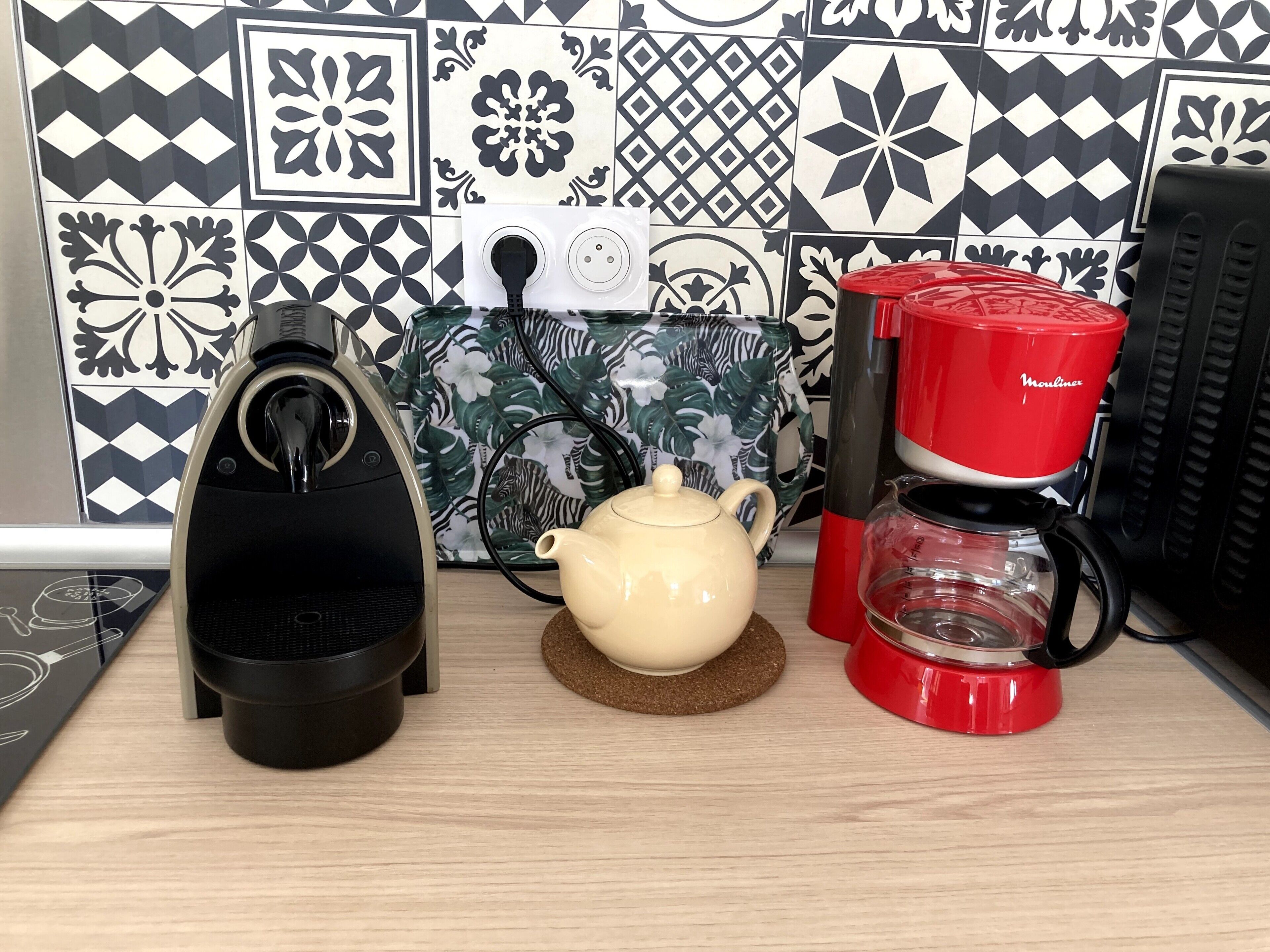 A kitchen with a coffee maker, kettle, and a patterned tile backsplash.