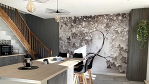 A modern kitchen with a wooden island, a dining area with chairs, a staircase, and a decorative wall.