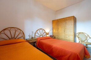A bedroom with two beds, a wardrobe, a nightstand, and a chair.