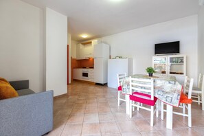 A modern kitchen with white cabinets, a dining table with chairs, and a TV mounted on the wall.