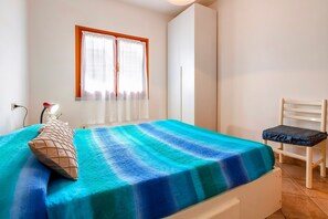 A bedroom with a bed, a chair, a wardrobe, and a window with curtains.