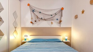 Un dormitorio con colcha a rayas, dos lámparas de noche, una red decorativa con conchas y estrellas, y un espejo montado en la pared.