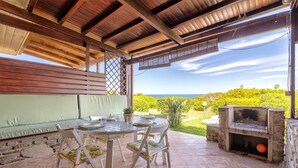 Patio esterno con tavolo e sedie, un forno in pietra e vista sull'oceano.