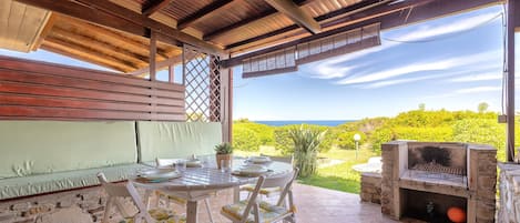 An outdoor patio with a table and chairs, a stone oven, and a view of the ocean.