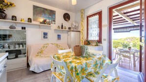 Una stanza con un letto, un tavolo da pranzo con sedie, un angolo cottura con scaffali e vista dalla finestra.