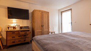Une chambre à coucher avec un lit, une commode en bois, une télévision et une porte avec des rideaux.