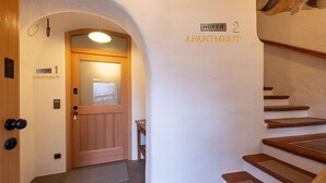 Un couloir d’hôtel avec une porte en bois portant l’inscription « APPARTEMENT HOFER 1 » et un escalier menant à « APPARTEMENT HOFER 2 ».