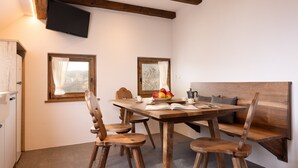 A dining area with a wooden table, chairs, a bench, and a television mounted on the wall. - Apartment 'Hofer Hitt 2' with Mountain View, Shared Garden and Wi-Fi (Klobenstein)