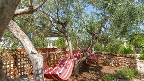A hammock tied to a tree in a garden with a stone wall and a wooden fence.