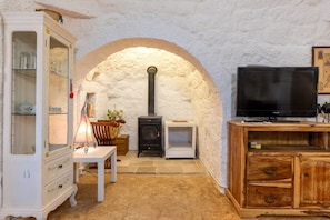 Un intérieur rustique avec une arche en pierre, un meuble blanc aux portes vitrées, un meuble TV en bois et une cheminée.