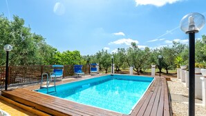 A rectangular swimming pool with a wooden deck, surrounded by a fence and trees.