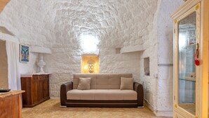 A room with a stone ceiling, a beige sofa, a wooden cabinet, and a glass cabinet with a red handle.