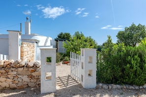 Un bâtiment blanc avec un mur en pierre, un chemin de gravier et une clôture blanche menant à un portail.