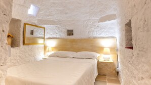 A room with a bed, a wooden headboard, a wall-mounted mirror, and a nightstand with a lamp.