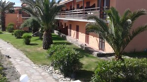 Un edificio de dos pisos con balcón, rodeado de palmeras y un sendero de piedra.