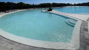 Una piscina grande y clara con cielo iluminado por el sol, rodeada de sillas de descanso y sombrillas.