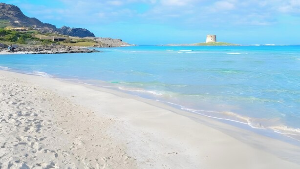Una playa con agua cristalina, una orilla de arena y una torre en una pequeña isla.