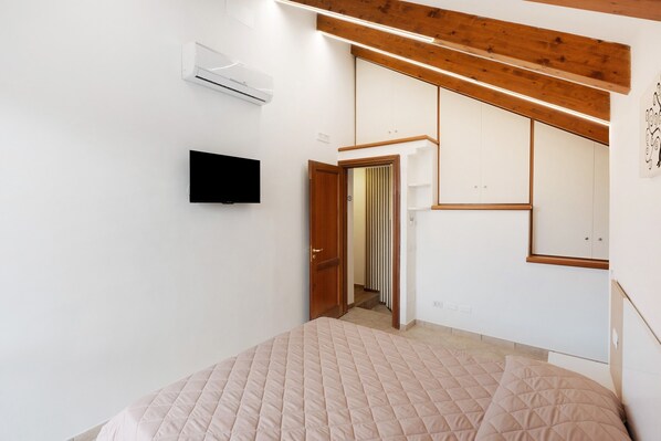 A bedroom with a bed, an air conditioner, a TV, and a wooden ceiling.