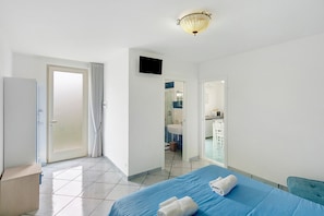 A hotel room with a bed, a television, a bathroom visible through an open door, and a ceiling light fixture.