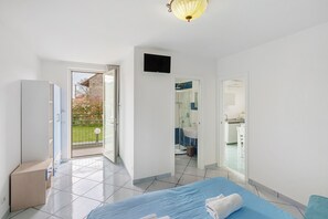 Un dormitorio con cama, armario, televisión y baño visible a través de una puerta abierta.