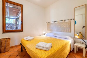 Une chambre à coucher avec un lit, une table de chevet, une lampe, une fenêtre et un miroir.