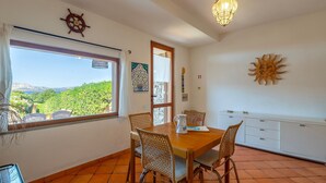 Un comedor con mesa, sillas, una jofaina y vistas al follaje exterior.