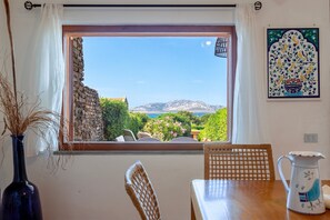 Une pièce avec vue sur les montagnes et la mer, une table avec des chaises, un vase contenant des plantes séchées et un carreau décoratif sur le mur.