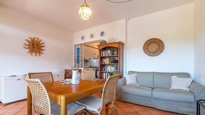 Un comedor con una mesa y sillas de madera, un sofá, una estantería y un adorno de sol en la pared.