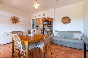 Un coin repas avec une table et des chaises en bois, un canapé, une bibliothèque et un soleil décoratif peint sur le mur.