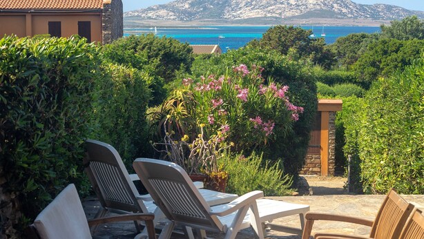 Un patio con sillas y una mesa, rodeado de follaje y vista al mar.