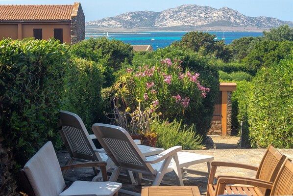 Une terrasse avec des chaises et une table, entourée de verdure et offrant une vue sur la mer.