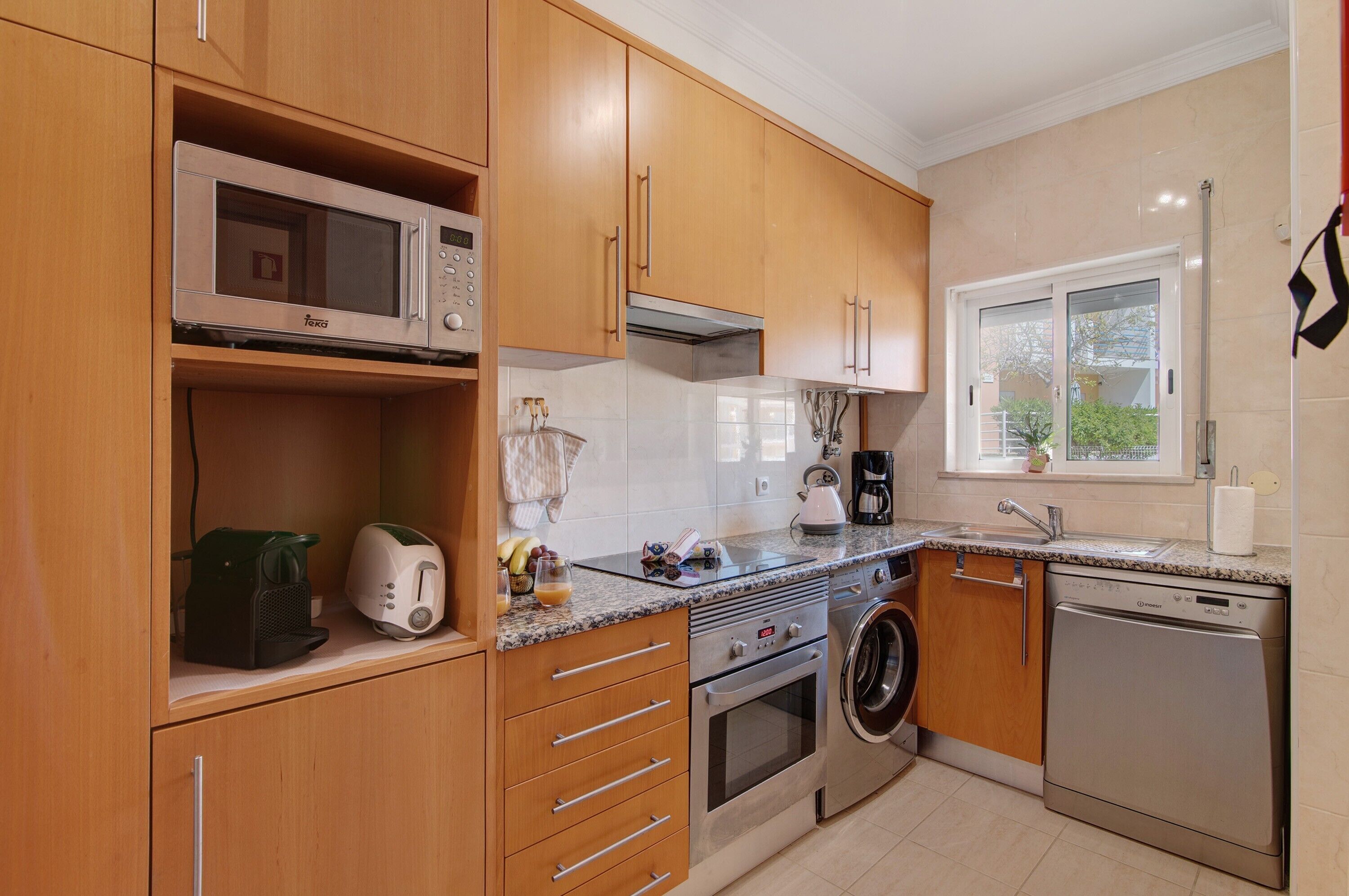 A modern kitchen with wooden cabinets, a microwave, a coffee maker, a kettle, and a dishwasher.