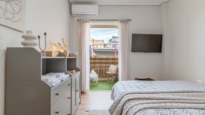 A bedroom with a bed, a dresser, a TV, and a view of a balcony with a chair and a small garden. - Apartment 'Meliti Kalamata' with Mountain View, Wi-Fi and Air Conditioning (Unknown)