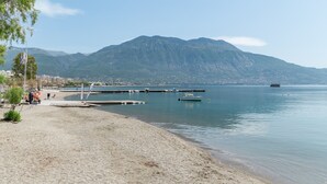 A beach with a mountain in the background, calm water, and a pier extending into the water. - Apartment 'Meliti Kalamata' with Mountain View, Wi-Fi and Air Conditioning (Unknown)