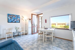 Une pièce avec un canapé bleu, une table à manger et des chaises, un tableau accroché au mur et une vue par la fenêtre.